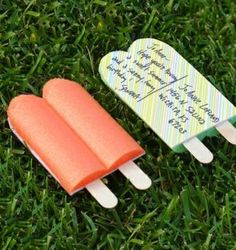 two popsicles sitting on top of green grass next to each other with writing on them