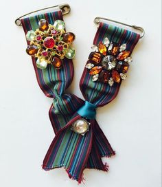 two pieces of colorful fabric with brooches and beads attached to each other on a white surface