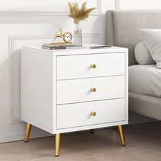 a white nightstand with two drawers and a clock on it's side next to a bed