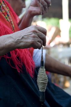 an old woman is holding a piece of string in her hand and weaving it with two hands