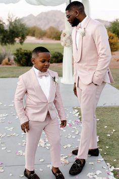 a young boy in a pink suit and bow tie standing next to an older man