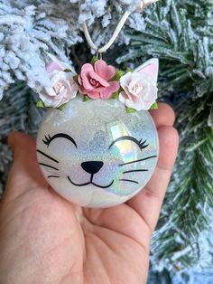 a hand holding a glass ornament with a cat face on it