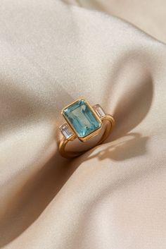 a ring with an aqua blue topazte surrounded by white diamonds on a silk background