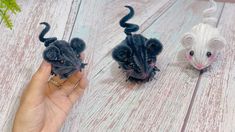 two stuffed mice are being held up by someone's hand on a wooden surface