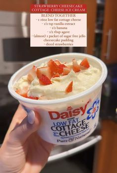 someone holding up a cup of ice cream with strawberries on top