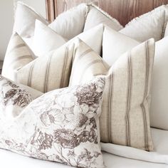 four pillows on top of a bed with white linens and brown floral print pillow cases