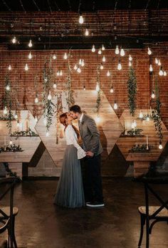 a man and woman kissing in front of a wall with lights