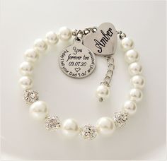 a white bracelet with two charms and a heart charm on the clasp that says, you forever love