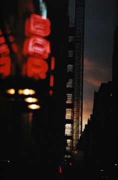 the city skyline is lit up at night with red neon signs in the foreground