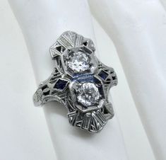 Thank you for viewing this beautiful antique Art Deco 1920's 18k white gold diamond and French cut sapphire ring.  The ring contains 2 old European cut diamonds weighting approximately .70 carats.  The diamonds are an average quality of G/H color and VS clarity.  The French cut sapphires are synthetic which were almost universally used in these type of rings from the time period.  The ring size is 4.75.  The weight of the ring is 3.2 grams.  The ring comes with an attractive gift box.  An import Antique Platinum Three-stone Jewelry, Art Deco Sapphire Diamond Ring In Diamond White, Art Deco Sapphire Diamond White Ring, Antique Silver Sapphire Diamond Ring, Vintage Diamond White Sapphire Jewelry, Antique Silver Diamond Ring With Sapphire, Art Deco Three Stone Platinum Jewelry, Antique Sapphire Diamond Ring In Silver, Antique Silver Sapphire Ring With Diamond Accents