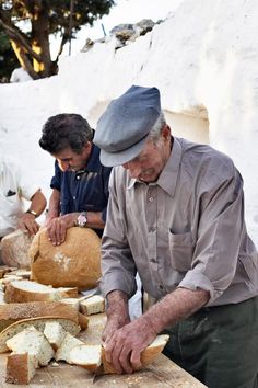 two men are cutting bread on a table