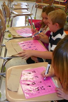 three children sitting at desks with pink paper on them