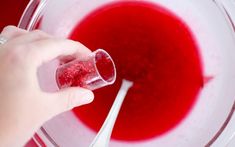 a hand holding a spoon over a bowl with red liquid