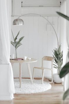 a table and chair in a white room with plants on the floor next to it