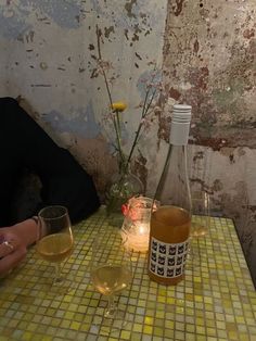 two glasses of wine on a table with a bottle and vase in the corner behind them