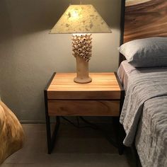 a lamp on a night stand next to a bed in a room with gray walls