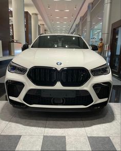 the front end of a white bmw suv in a showroom with people looking at it