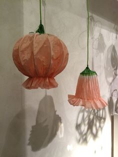 three paper lanterns hanging from the ceiling in front of a wall with shadows on it