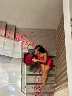 a woman in a red dress is sitting on stairs with flowers and a handbag