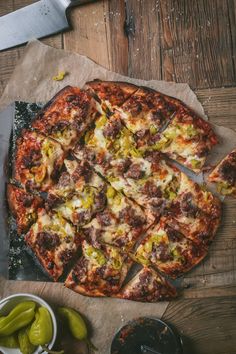 a pizza sitting on top of a wooden table next to green peppers and a knife