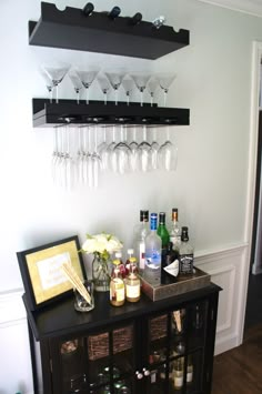 a bar with wine glasses and liquor bottles on the top shelf, next to a framed photograph