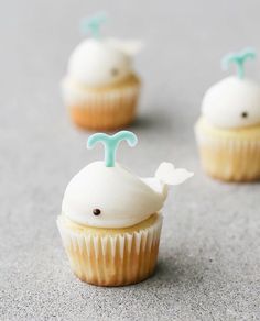 three cupcakes with white frosting and blue icing on the top one is shaped like a whale