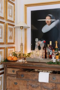 an old dresser with liquor bottles and glasses on it in front of a framed portrait