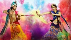 two women dressed in colorful costumes dancing with colored powder on their faces and arms, both holding hands