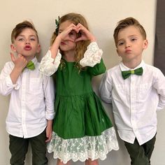 three young children standing next to each other in front of a white wall wearing green bow ties