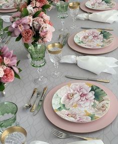 the table is set with pink and green plates, silverware, and floral centerpieces