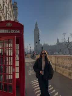 a woman standing next to a red phone booth