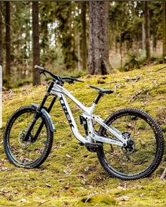 a white mountain bike parked in the grass near some trees and a sign with words on it