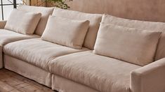 a beige couch with several pillows on it in front of a window and wooden floor