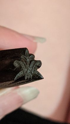 a woman's hand holding a small piece of black metal with fleur de lis on it