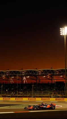 a red race car driving down a track at night with stadium lights in the background