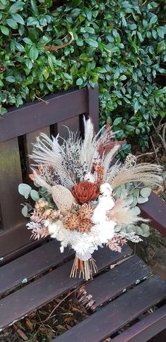 a bouquet of flowers sitting on top of a wooden bench next to a bush and shrubbery