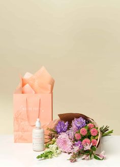 a bouquet of flowers sitting next to a pink gift bag and bottle of lotion