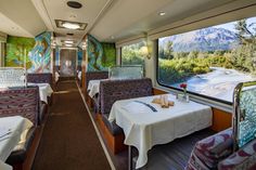 the inside of a train car with tables and chairs on it, along with mountains in the background