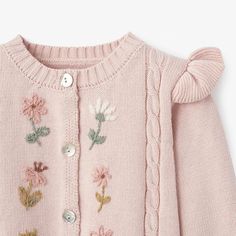 a pink sweater with flowers and buttons on the front is shown in close up view