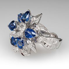 This impressive cluster style ring is accented with three (3), prong set, oval mixed cut natural sapphires, two (2), prong set, pear mixed cut natural sapphires and one (1), prong set, triangular mixed cut natural sapphire. The sapphires are bordered with four (4), prong set, round brilliant cut diamonds and twenty- eight (28), bead set, round brilliant/single cut diamonds, bordered with milgrain edging. Engraved details accent the shoulders of the shank. The ring measures 22.5mm at the top, rises 10.1mm above the finger, tapering to 3.6mm wide and 1.2mm thick at the base of the shank. This ring is currently a size 6.75. Luxury Sapphire Cluster Ring With Brilliant Cut, Luxury Sapphire Cluster Ring, Luxury Classic Sapphire Cluster Ring, Luxury Multi-stone Cluster Sapphire Ring, Elegant Cluster Sapphire Ring, Gia Certified, Blue Sapphire Diamond, Natural Sapphire, Diamond Cluster, Round Brilliant