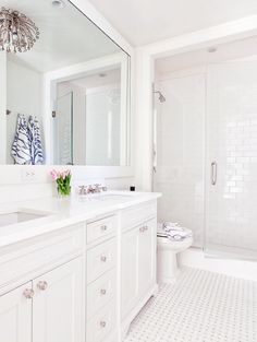 a white bathroom with a large mirror above the bathtub and shower area, along with two sinks