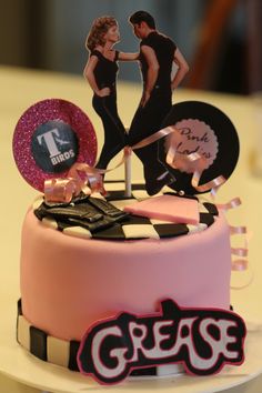 a cake with two people on top and the words grease spelled out in black letters