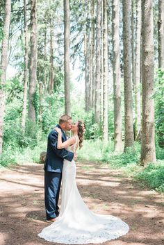 a bride and groom standing in the middle of a wooded area with their arms around each other