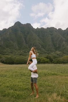 a man and woman are playing frisbee in a field with mountains in the background