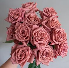 a bouquet of pink roses is held in someone's hand with green leaves on it