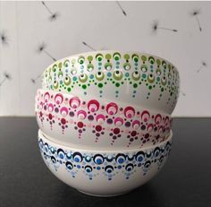 three colorful bowls sitting on top of a black table next to dandelions in the background