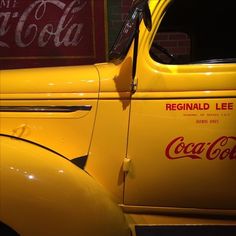 an old yellow truck parked next to a coca cola sign