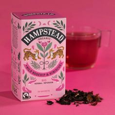 a box of tea next to a cup of tea on a pink background with the word hampstead