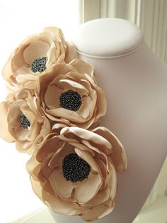 three large flowers are attached to a mannequin's neck piece, with black beads in the center