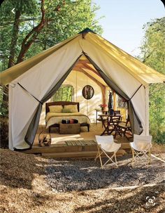 a tent is set up in the woods with two chairs and a bed inside it